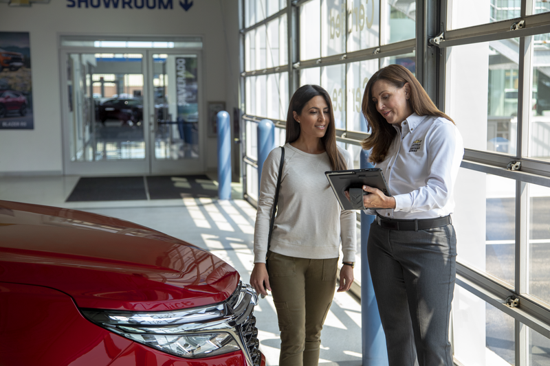 Chevrolet certified service technician is showing her ipad to the cutomer, a woman, in the dealership showroom
