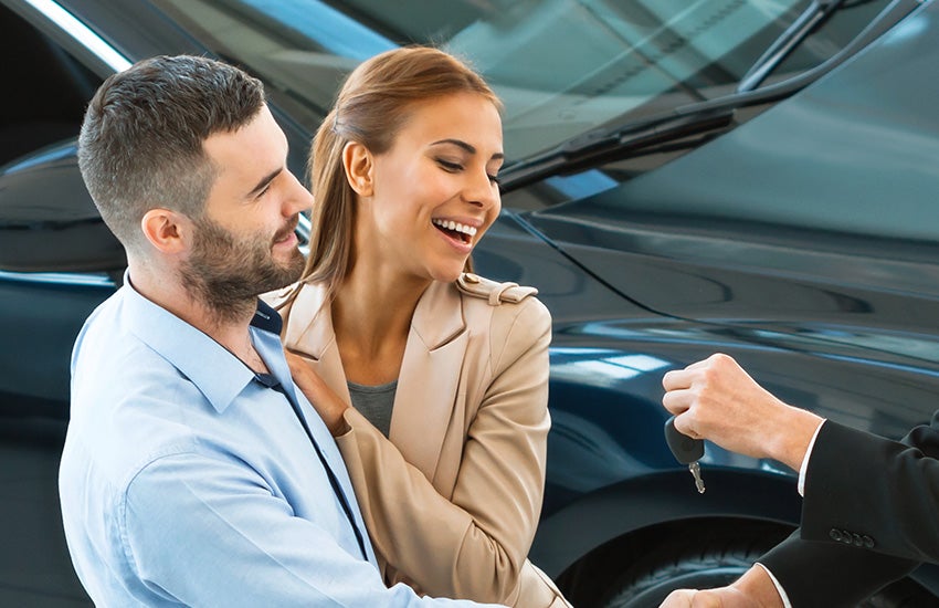 Image of a couple smiling and looking at the key being offered by the dealer inside the dealership